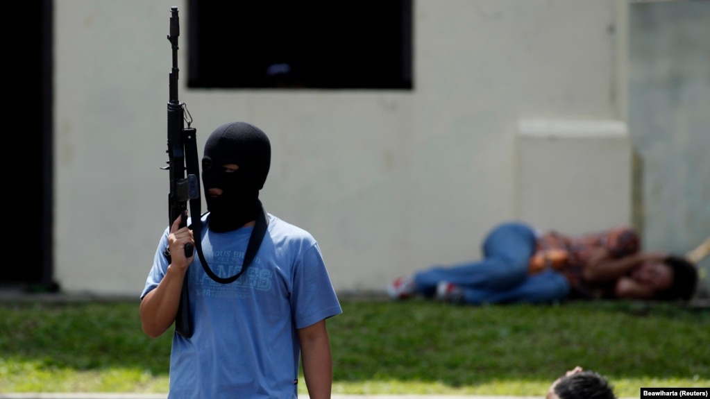 Seorang teroris tiruan memegang senapan di dekat "warga sipil yang ditahan" dalam latihan anti-teror di markas pasukan khusus polisi di Depok, Jawa Barat, 9 Maret 2010. (Foto: REUTERS/Beawiharta)